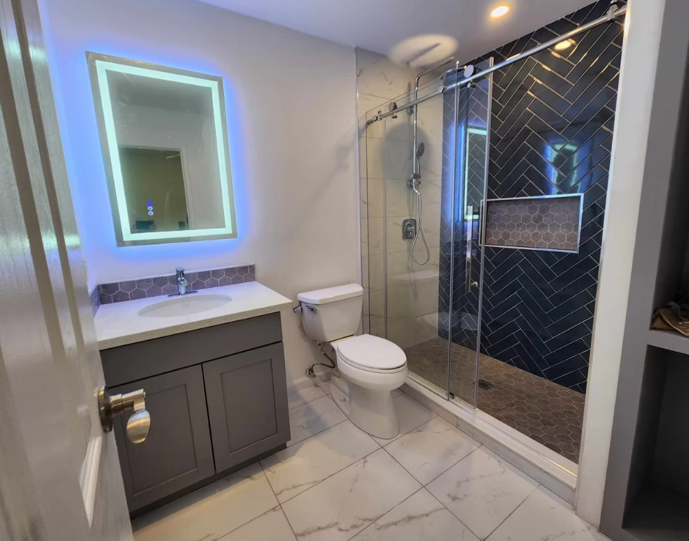 Walk-in shower with black herringbone tile and LED-backlit mirror, installed for a homeowner in Redmond